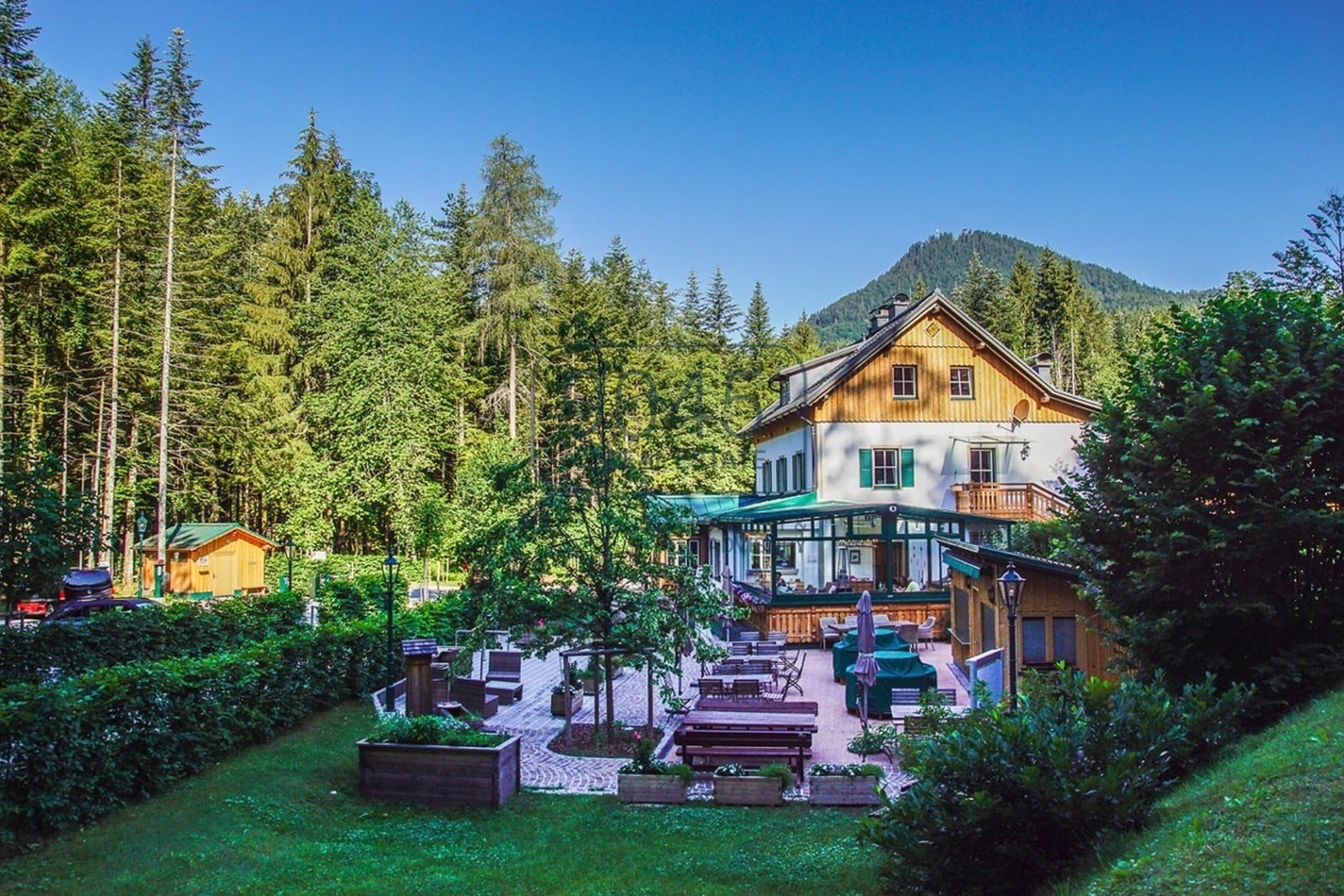 Landhaus mit Holzgiebel, grünen Fensterläden und Wintergarten vor Fichtenwald und bewaldetem Berg im steirischen Ausseerland