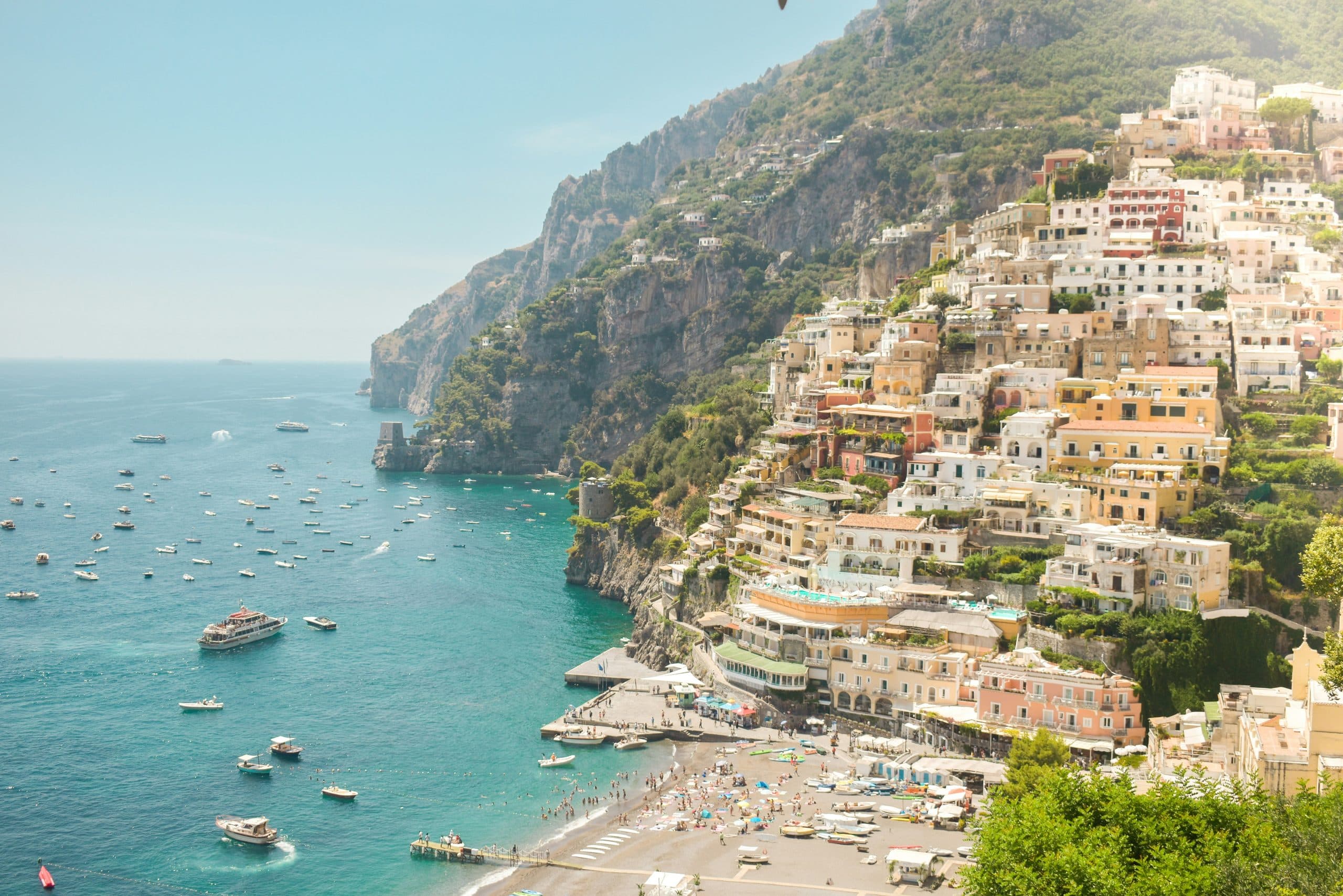 Bunte Häuser von Positano am Steilhang der Amalfiküste über dem türkisblauen Meer mit Booten in der Bucht