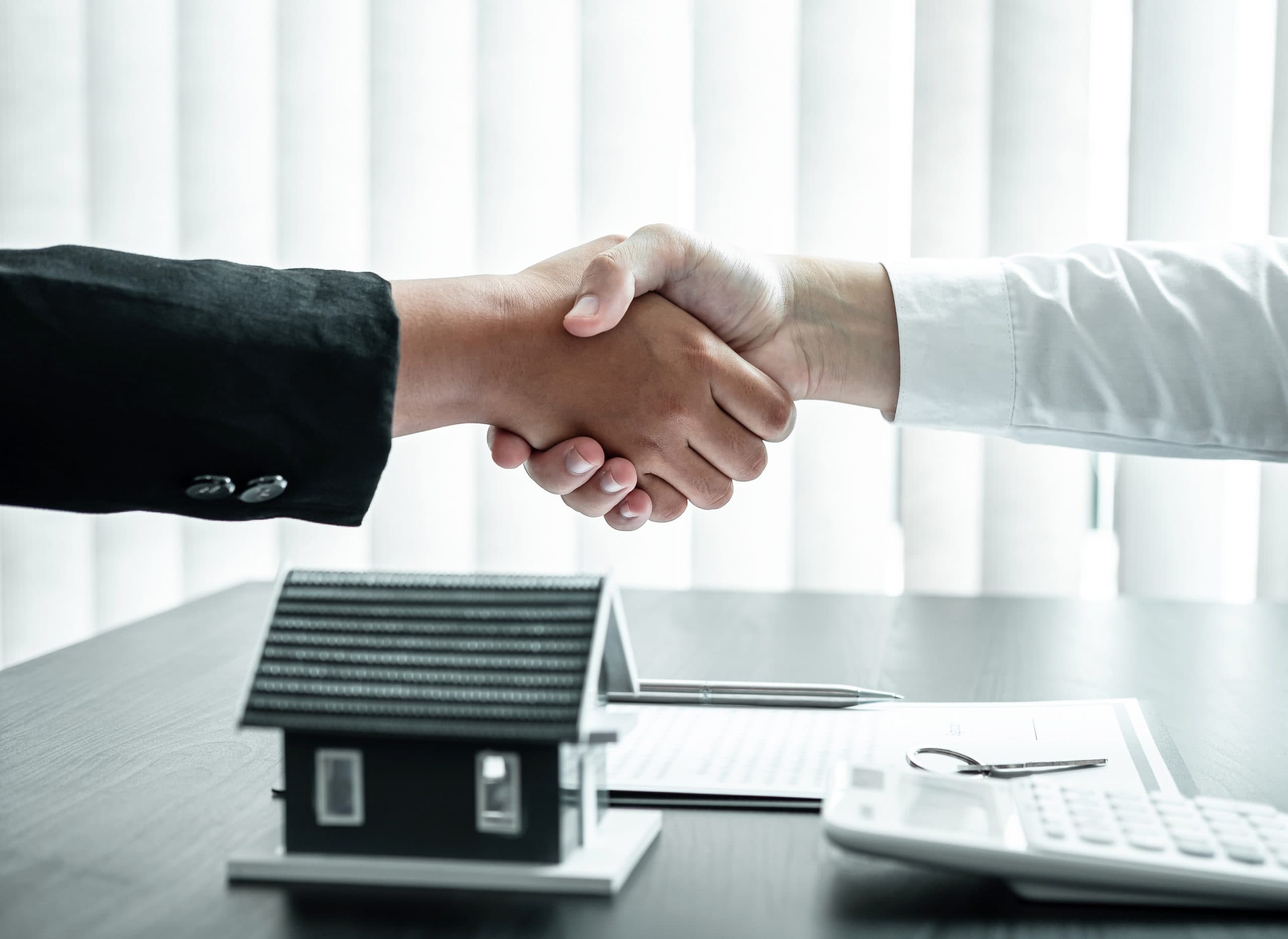 Handshake with a partner over a desk holding a model house and keys