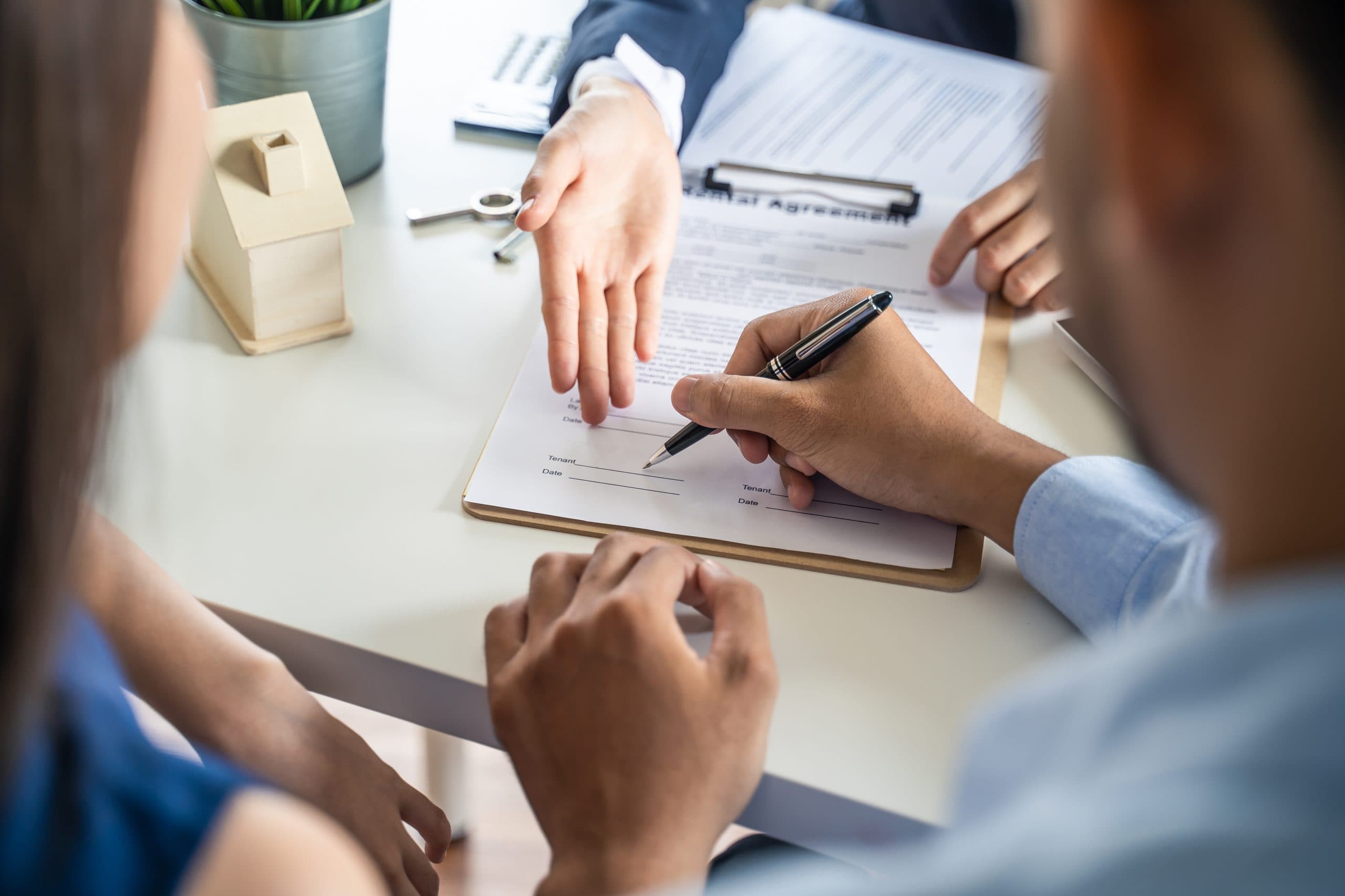 Couple signing a contract while the agent points at the relevant clause