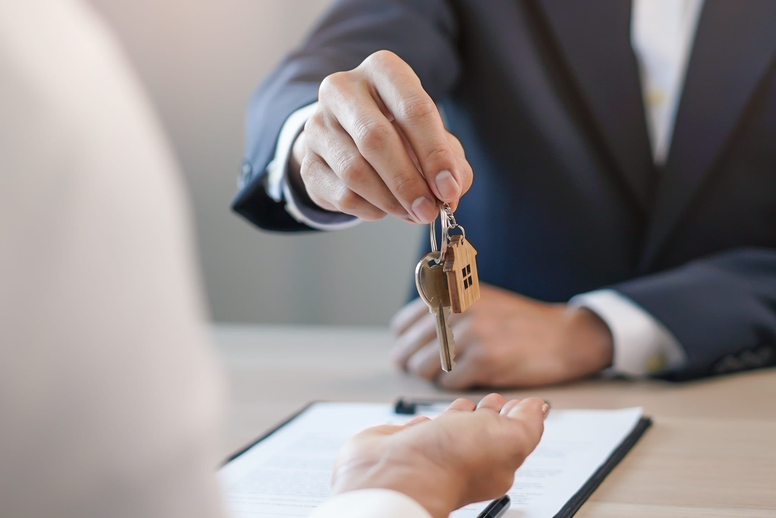 Agent handing over the house key with a house shaped fob across the desk