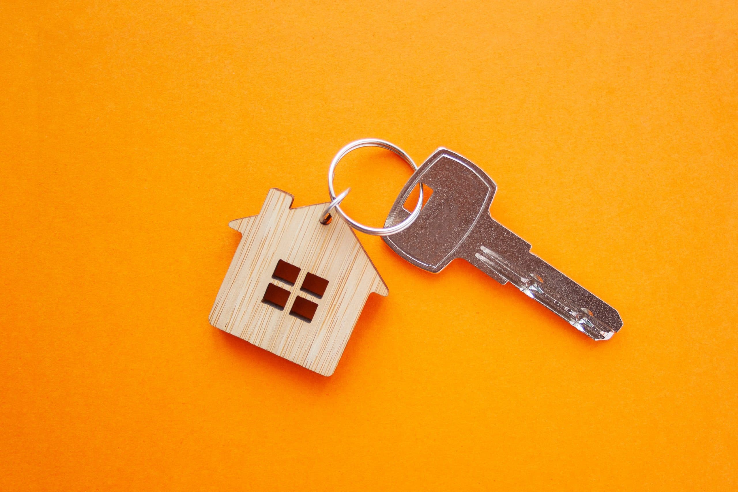 Key with a wooden house shaped fob on an orange background for letting